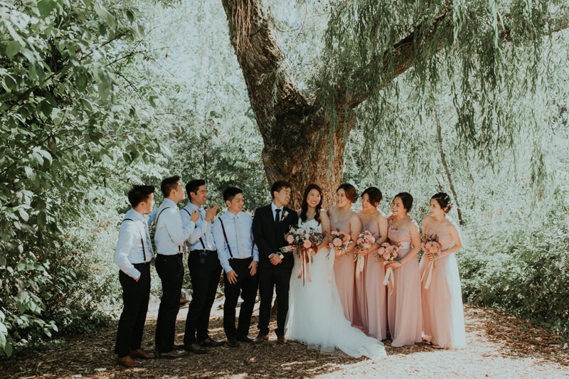 Modern PNW wedding party under a weeping willow tree, with groomsmen in blue and bridesmaids in pink.
