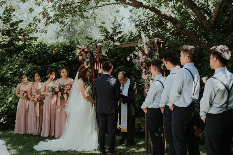 Beautiful garden wedding ceremony at Robinswood House, with bridesmaids in soft pink and groomsmen in light blue. 