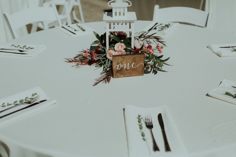 Garden style wedding centerpiece, with pink florals in a white lantern, and wooden table number. 