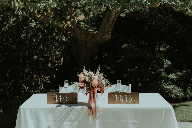 Sweetheart table with wooden Mr. and Mrs. signs, and pink bouquet.