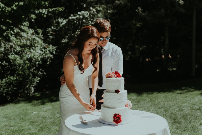 Modern bride and groom cut the cake, with bride in a mermaid gown with sweetheart neckline.