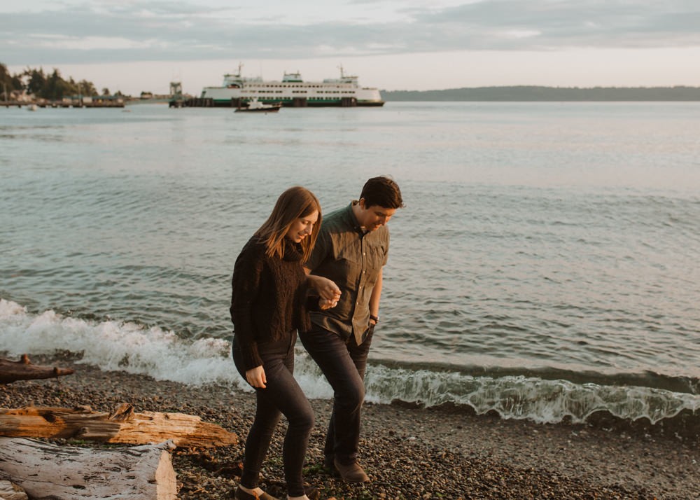 Engaged couple on the beach at sunset, with a ferry in the background. 