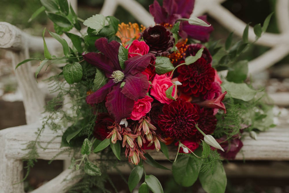 Modern wedding bouquet with deep purple, bright pink, and orange flowers like clematis, dahlias, and ranunculus. 