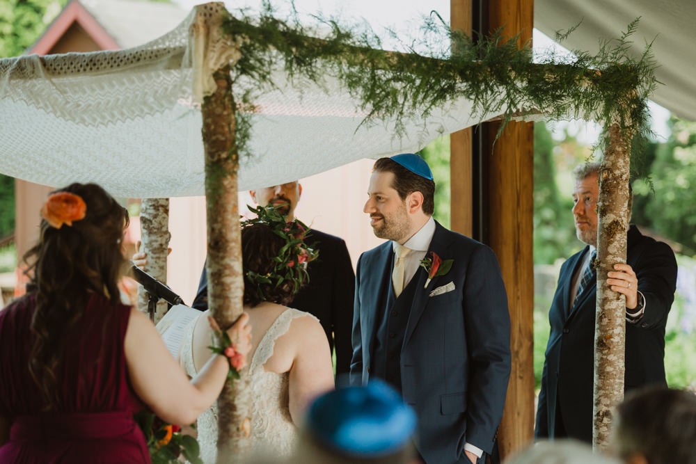 Bride and groom under chuppah with baby ferns and knit fabric. 