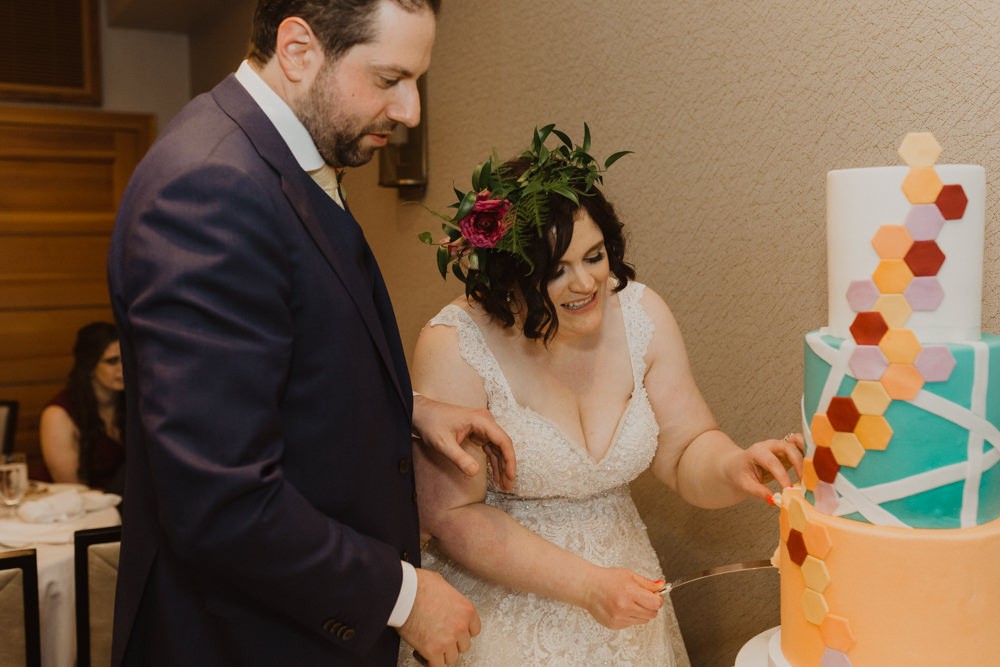 Bride and groom cut colorful geometric wedding cake. 