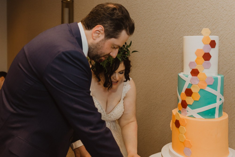 Colorful geometric wedding cake cutting by bride and groom. 