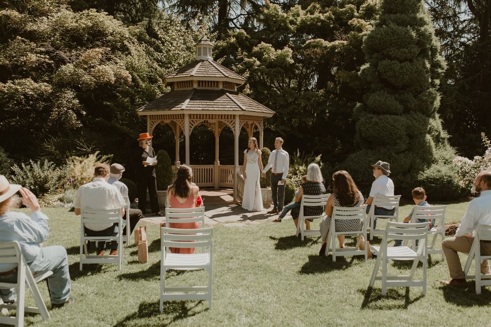 Wedding ceremony at the Woodland Park Rose Garden gazebo, with guests socially-distanced and masked. 
