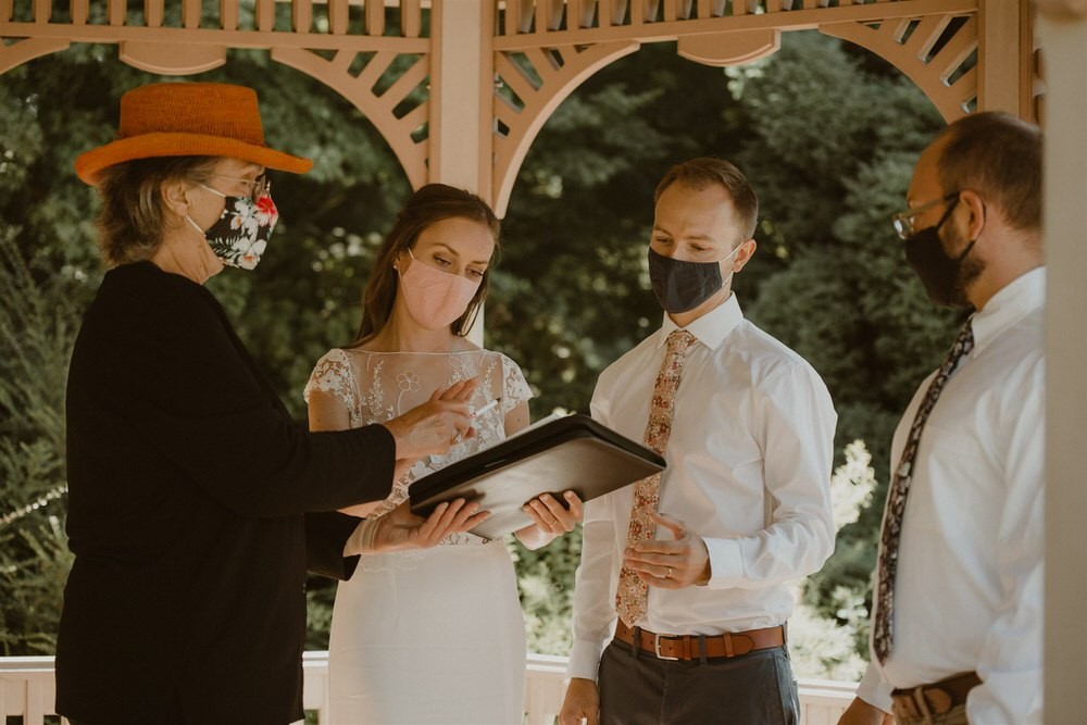 Small socially-distanced wedding ceremony with bride, groom, and guests wearing masks. 