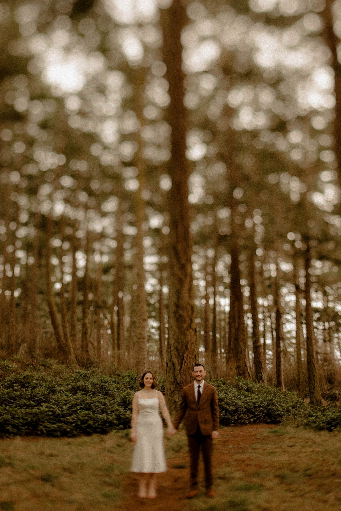Eloping couple holding hands on a rainy winter day in a dewy forest at Deception Pass. 