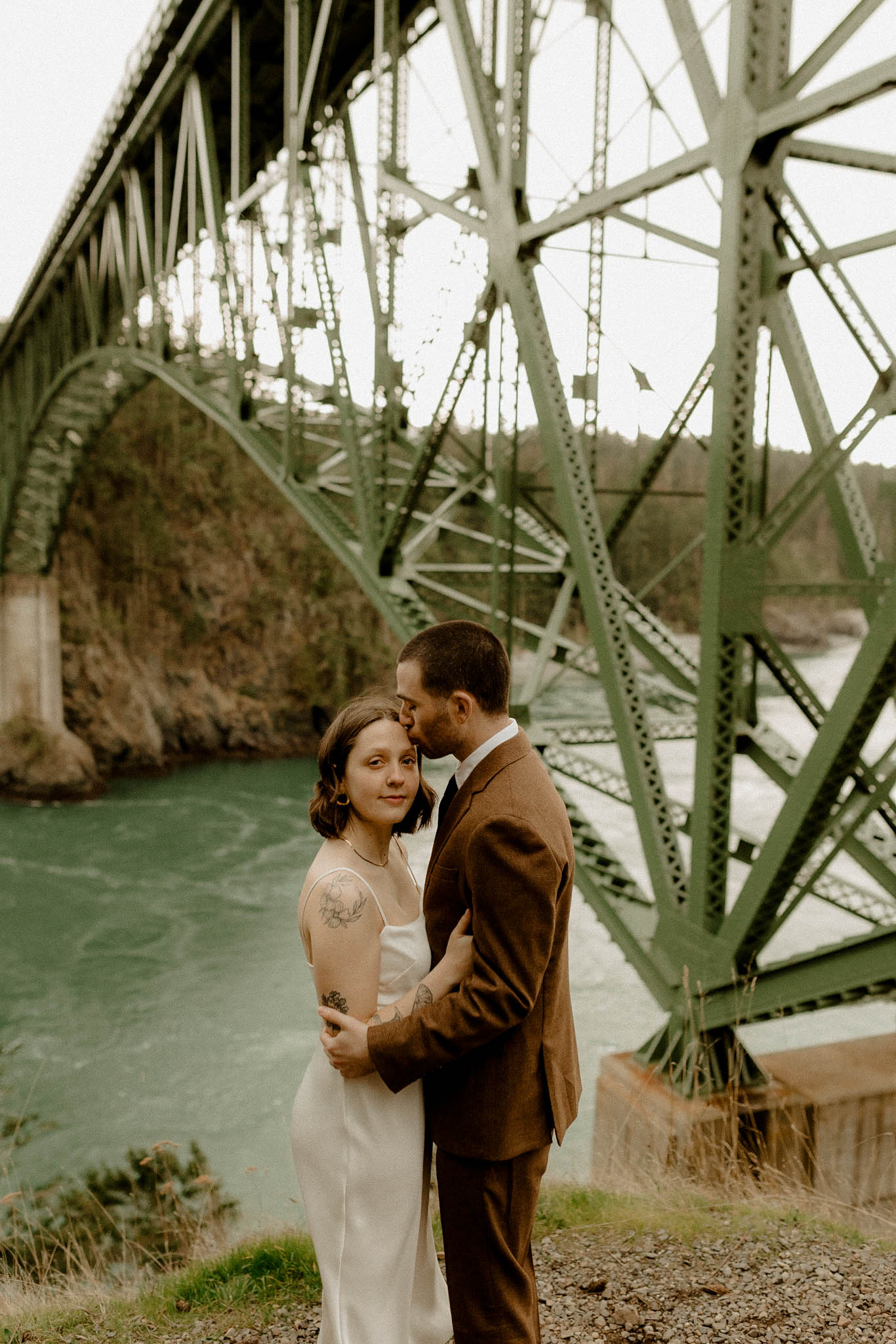 Eloping couple hugging in front of Deception Pass Bridge and water. 
