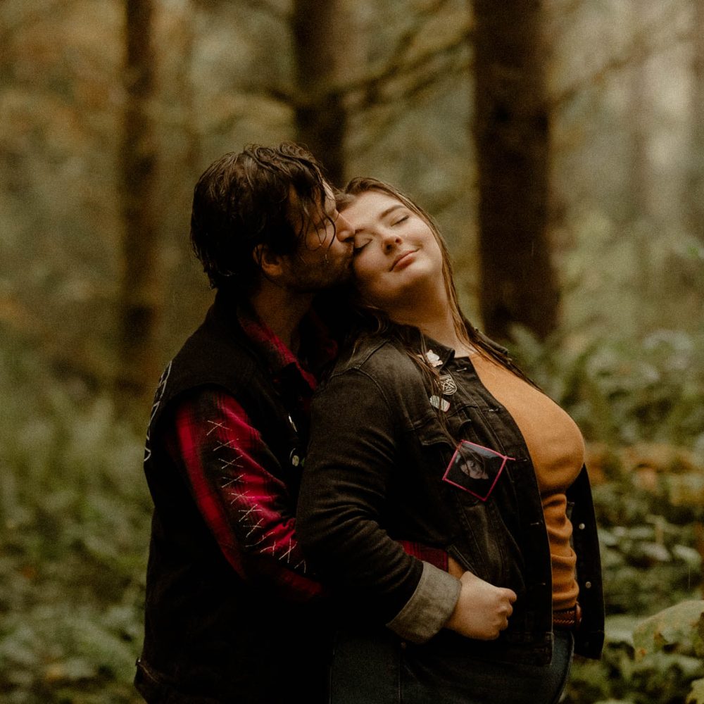 A rainy engagement session in a Poulsbo forest with couple dressed in casual punk outfits.